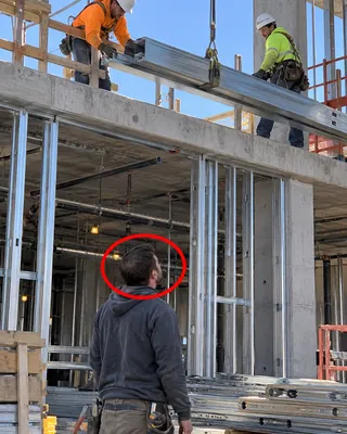 Site photo circled in red: ground-level worker beneath suspended steel beam without visible hard hat